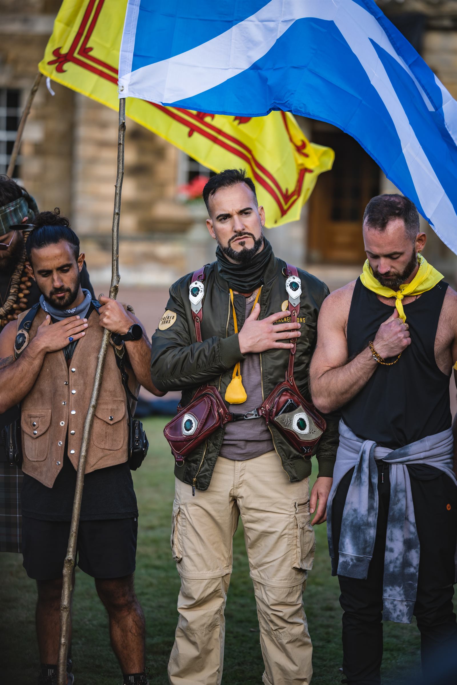 Pierre et deux hommes, main sur le cœur, devant un drapeau écossais